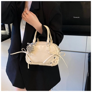 Détail du sac Boston crème avec nœud latéral et pendentif cœur porté par le mannequin