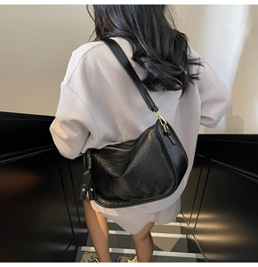 Detail of a black pleated leather crescent bag on model showing texture and drape