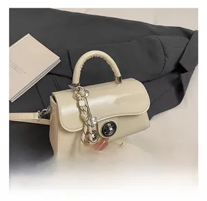 Détail du petit sac en cuir verni crème avec fermoir rotatif argenté et charm