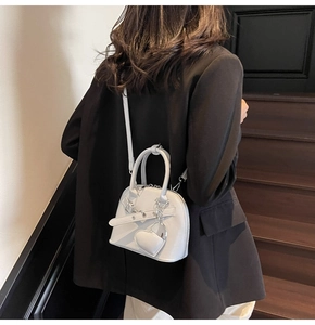 Detail of light gray shell bag featuring leather strap and heart pendant on model