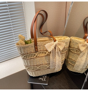Close-up of woven straw tote bag with brown leather handles and large lace bow detail