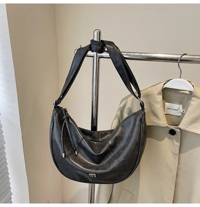 Détail du sac croissant en cuir noir avec bandoulière nouée et logo argenté sur trench-coat