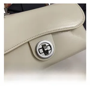 Gros plan du fermoir en métal argenté et des coutures sur le petit sac carré blanc crème