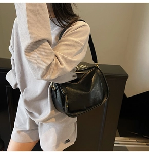 Detail of a black faux leather underarm bag featuring unique pleated texture and gold zipper