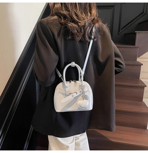 Detailed back view of a light gray shell bag worn with a chic black suit on stairs
