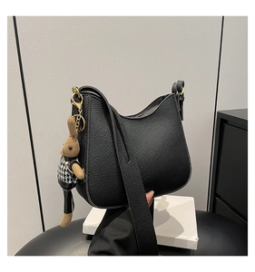 Detail of black lychee grain leather bucket bag with gold hardware and rabbit plush pendant