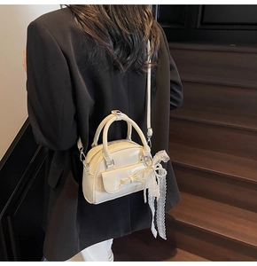 Detail of cream white glossy bowling bag with lace pearl charm and leather bow