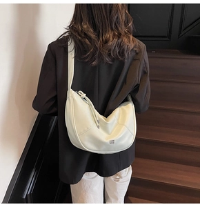 Détail d'un sac à bandoulière demi-lune beige avec coutures latérales et tirettes de zip nouées