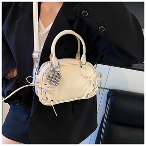 Détail du sac Boston crème avec pendentif cœur argenté et texture lisse et brillante