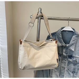 Close-up of cream canvas tote bag with brown leather details on a hanging rack