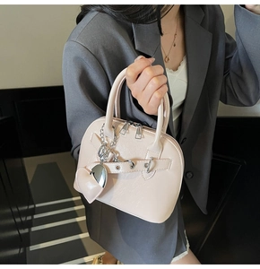 Close-up of shell-shaped handbag in beige pink with heart charm and silver chain detail