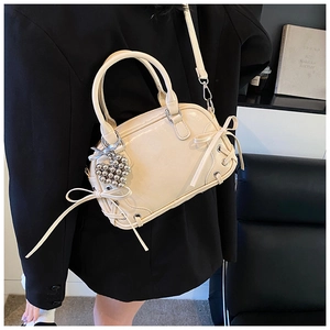 Détail du sac Boston crème avec nœuds latéraux et pendentif cœur argenté