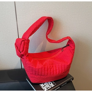 Detailed shot of red quilted nylon shoulder bag with stylish knot strap on a book