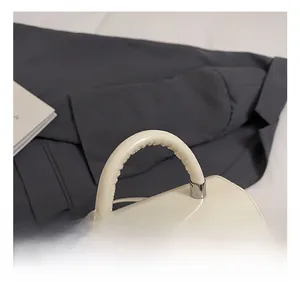 Détail d'un sac à main crème brillant avec nœud tressé et breloque argentée
