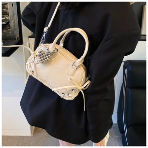 Détail du sac Boston crème avec nœud et breloque cœur sur une veste de blazer noire