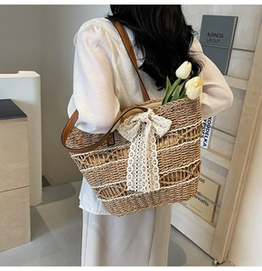 Detail of hand-woven straw tote with white lace bow and leather straps on model