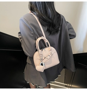Detail of light pink shell bag with heart charm and silver chain on model in gray blazer