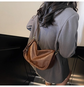 Detail of dark brown leather crescent bag with gold buckle and tassel zipper on model