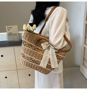 Close-up of natural straw tote bag with white lace bow and brown leather shoulder strap