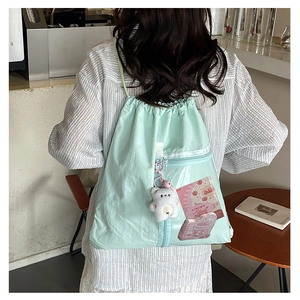 Detail of mint green canvas drawstring backpack with clear front pocket and bear charm