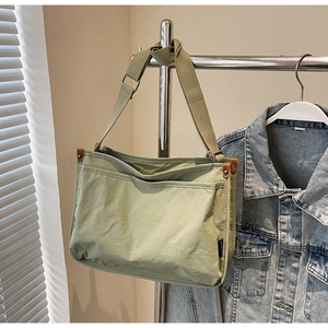 Close-up of sage green canvas tote bag with woven strap and metal fastener detail