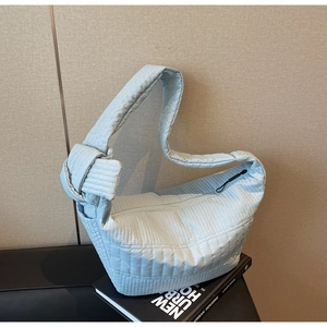 Detail of light blue quilted tote bag showing knot strap design on a textured background