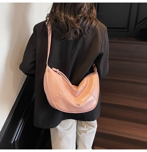 Sac bandoulière demi-lune rose porté par un mannequin avec cuir souple et logo métallique chic
