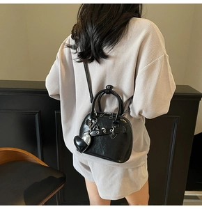 Detail view of black patent leather shell bag with heart charm on a crossbody strap