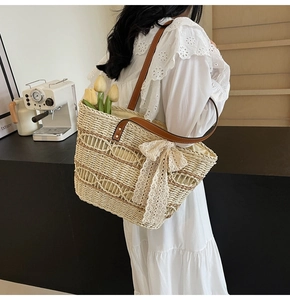 Close-up of woven straw tote bag featuring brown leather straps and white lace bow detail