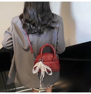 Close-up of a glossy red bowling bag with a lace bow and pearl pendant on a model
