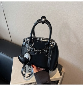 Detail of glossy black shell bag with silver heart charm and metallic chain accent