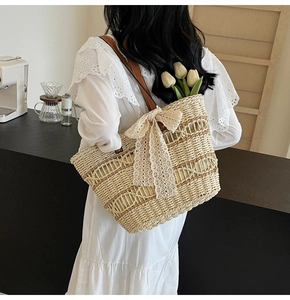 Detail of straw woven tote bag featuring beige lace bow and brown leather strap