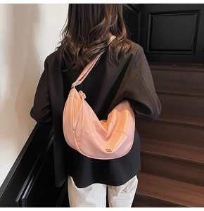 Sac à bandoulière rose en cuir brillant porté par un mannequin en costume noir