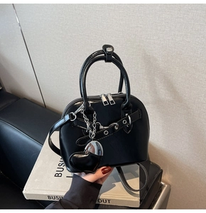 Detail of glossy black shell bag featuring a large silver heart pendant and metal eyelets