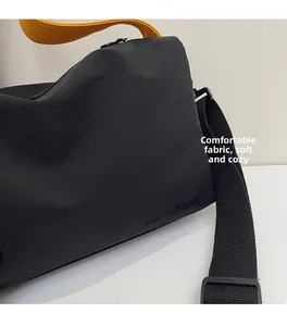 Détail du sac bandoulière en toile noire souple avec une poignée jaune éclatante