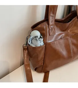 Close-up of the functional side pocket on a brown leather tote bag holding a folding umbrella