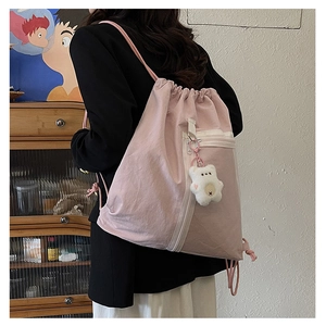 Pink drawstring backpack with white zipper pocket and plush bear charm on a model