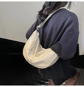 Détail d'un sac hobo crème avec logo métallique latéral et bandoulière réglable