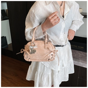 Détail du sac Boston rose en cuir avec nœud décoratif et pendentif cœur argenté