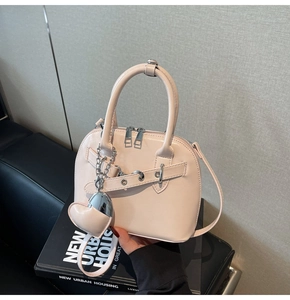Detail of pink shell-shaped crossbody bag with heart pendant and metallic chain trim