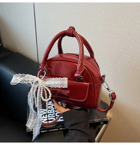 Detail of red glossy bowling bag featuring a bow pocket and elegant pearl lace charm