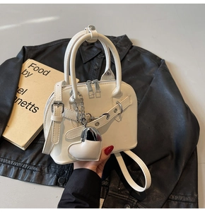 Detail of white shell handbag with silver chains, dual zippers, and heart charm accessory