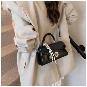 Détail d'un sac à main en cuir verni noir avec fermoir rotatif argenté et pendentif clochette