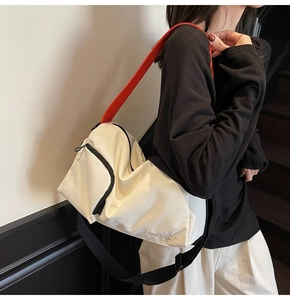 Détail d'un sac bandoulière en toile blanche avec sangle noire et poignée orange