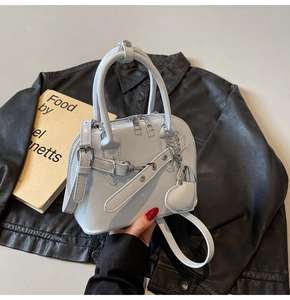 Detail of light gray shell bag with heart charm on black leather jacket background