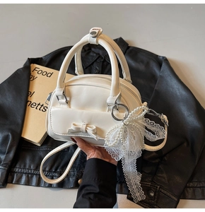 Detail of white bowling bag with bow pocket and elegant pearl lace charm on dark background