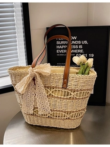 Woven straw beach tote bag with brown leather handles and a delicate lace bow detail