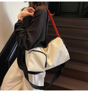 Détail du sac Boston en toile avec tissu blanc cassé, poignées rouges et bandoulière