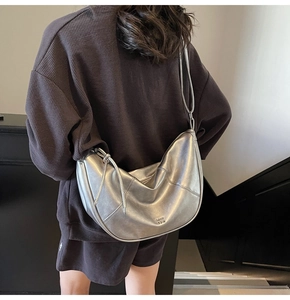 Détail du sac croissant argenté avec surpiqûres décoratives et logo embossé sur fini métal