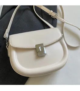 Detail of minimalist beige saddle bag featuring a polished silver rectangular metal lock